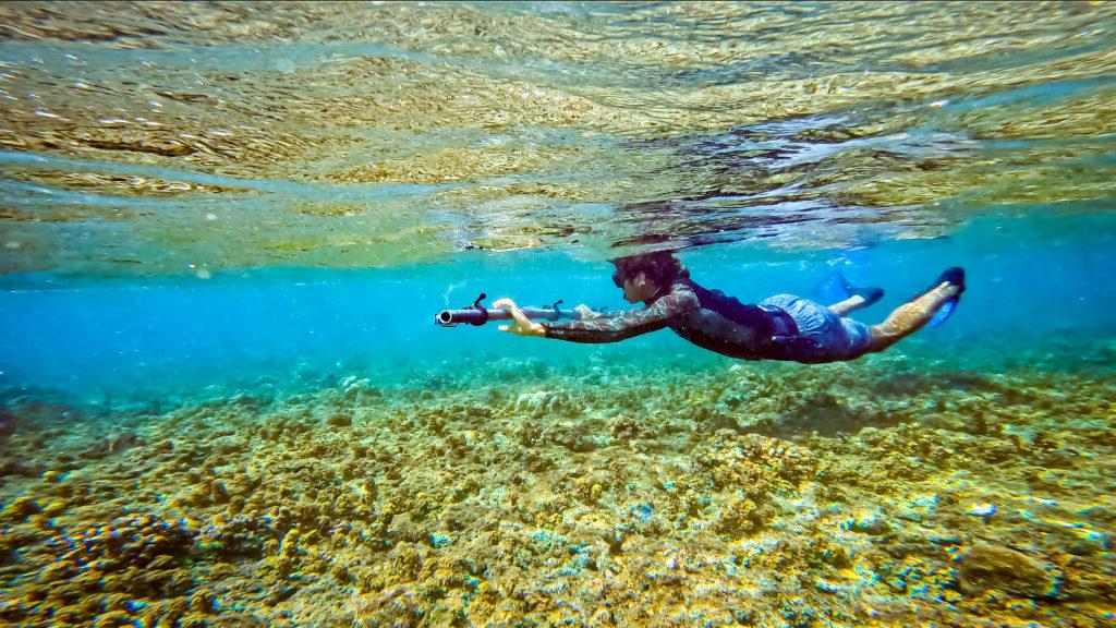 An underwater photo of Sammy Basa in snorkeling gear as he swims above the coral reefs in Sibuyan and holds out a surveying tool.